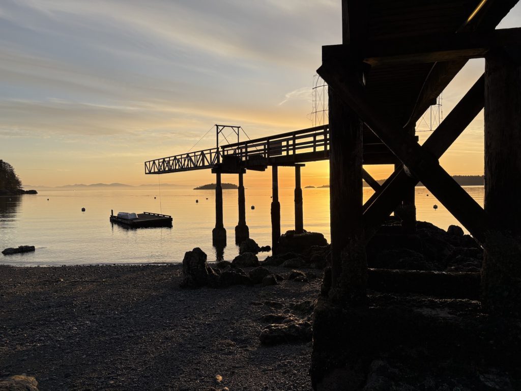 sunset pier over beach at low tide with dock and islands in background.