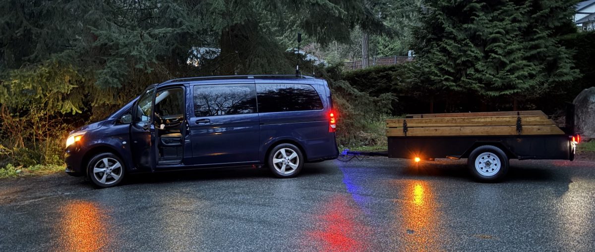 blue van pulls a black and wooden trailer